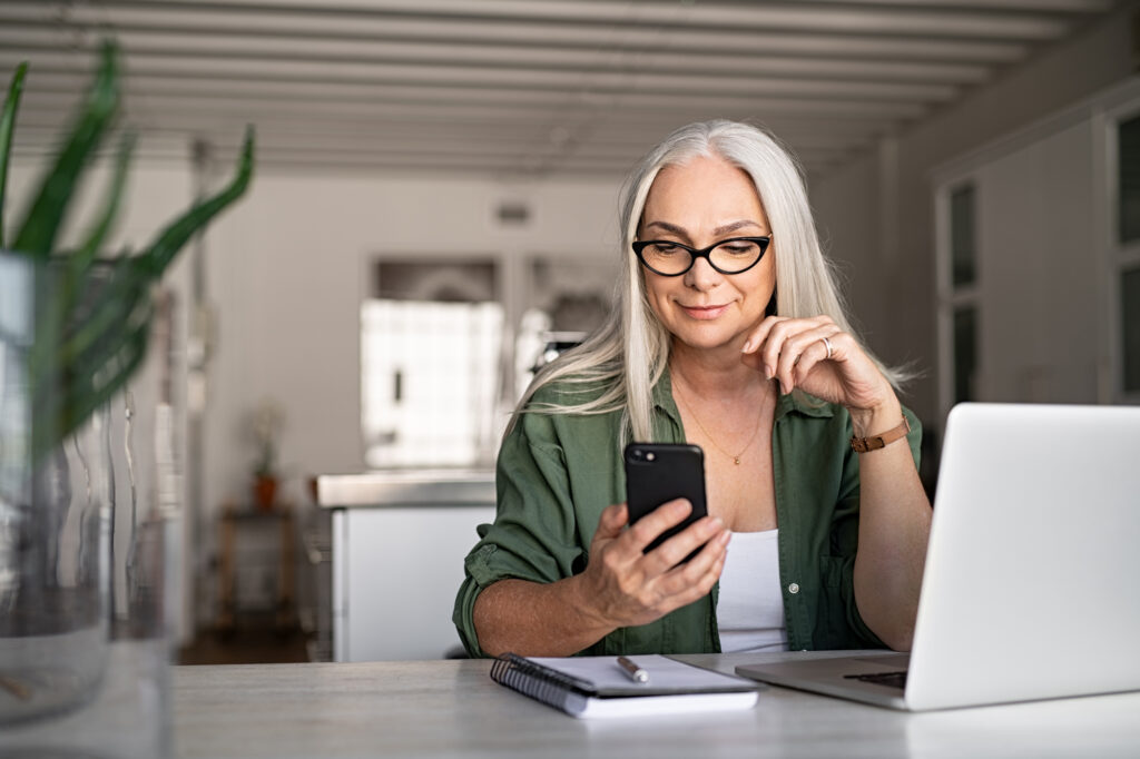 older woman working on computer holding phone