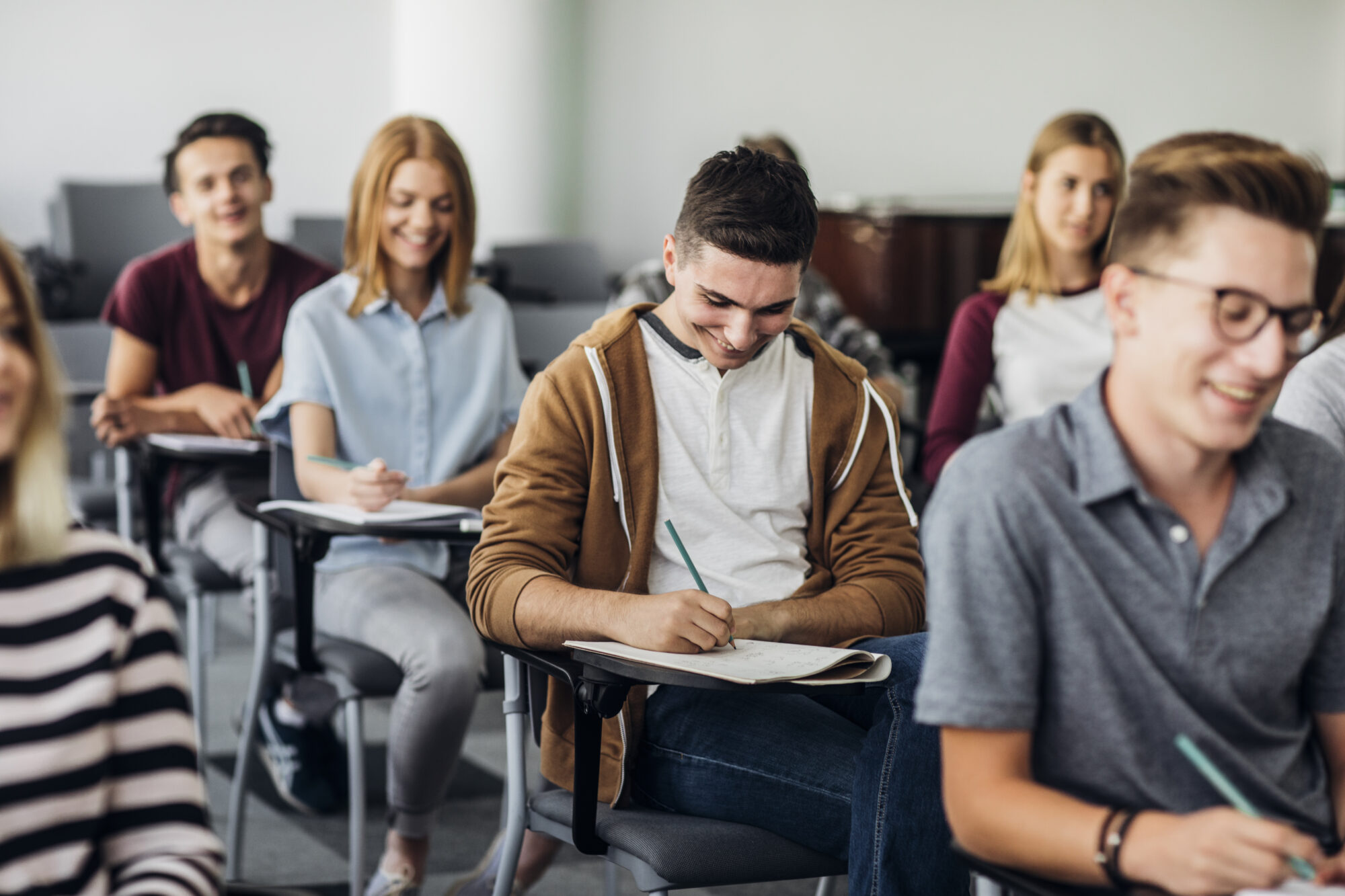 A group of students sits in a classroom, attentively taking notes. Everyone appears engaged and smiling, suggesting a positive learning environment enhanced by secure access control for schools. Desks and chairs are arranged in rows.