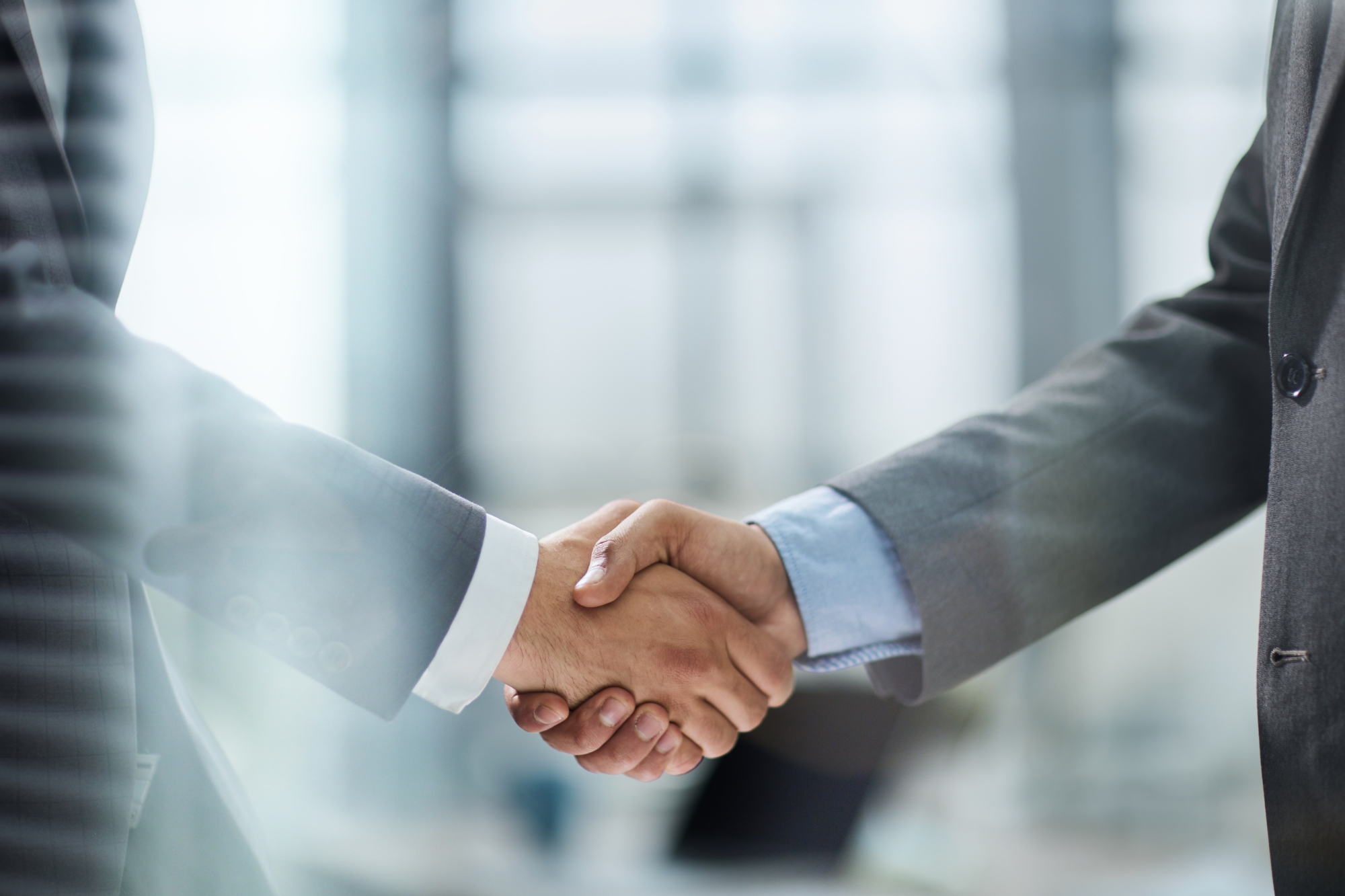 Two people in business suits shaking hands, symbolizing agreement or partnership in a Monolith to Microservices transformation, with a blurred office background.
