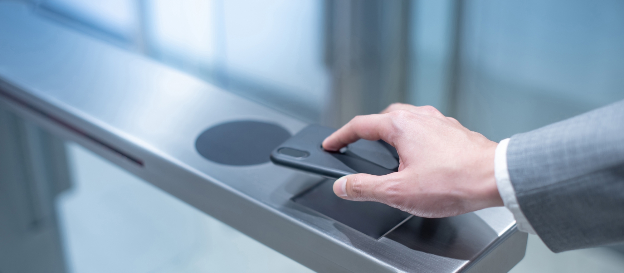 A person in a suit jacket uses web-based provisioning to tap their smartphone against an electronic turnstile reader.